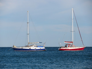 Two anchored yachts with deflated sails on the sea 