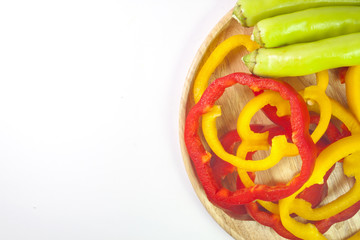 Fresh yellow and red pepper slices with green pepper in wooden plate on white background