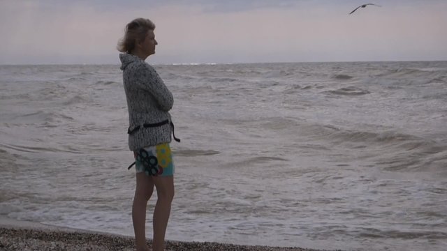 A woman stands on the seashore and thoughtfully sadly looking into the distance