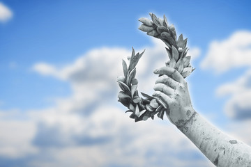 Laurel wreath hand held by a bronze statue on sky background