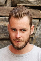 Fototapeta premium Attractive man wearing a grey sweater standing in front of a wall outside on a sunny summer day. 