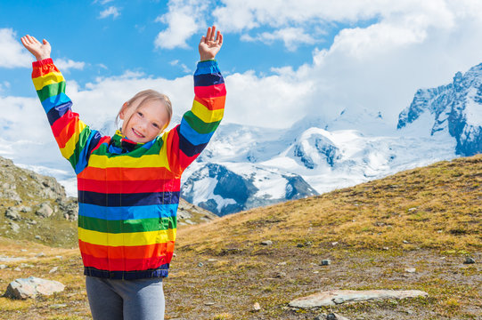 Cute little girl with arms wide open, wearing colorful coat, standing in front of Gornergrat glacier, Switzerland