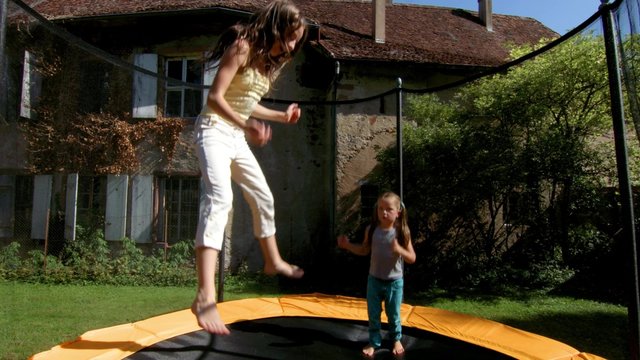 Two sisters jumping on the trampoline in backyard