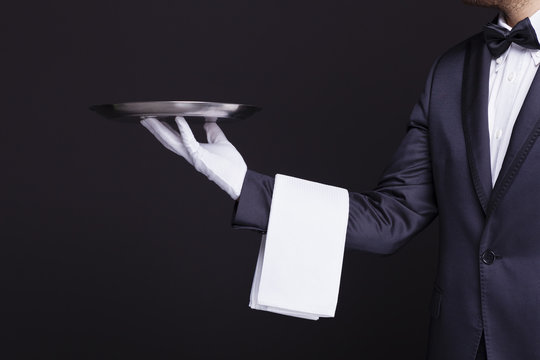 Waiter holding an empty silver tray against dark background