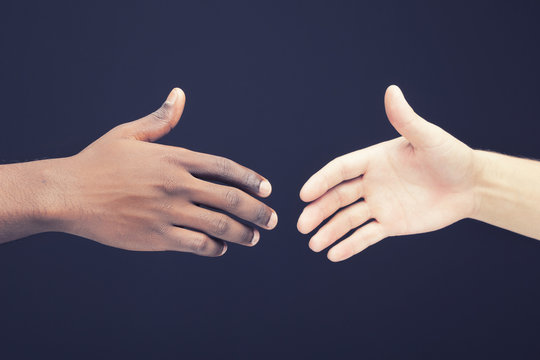 African and a caucasian man shaking hands over dark background