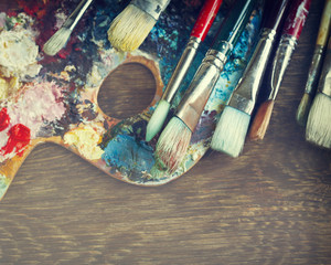 Artist paint brushes and palette on wooden background. Toned image