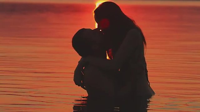 Romantic kiss in the water on a background sunset