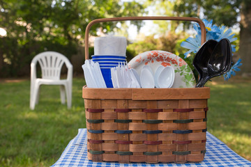 Summer day picnic basket with plastic cutlery and paper plates in outdoor setting