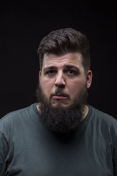 Confused young man with big beard, black background.