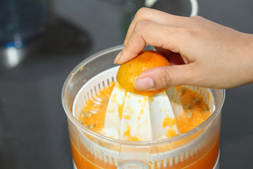 orange fruit squeezed with woman hand in juicer machine