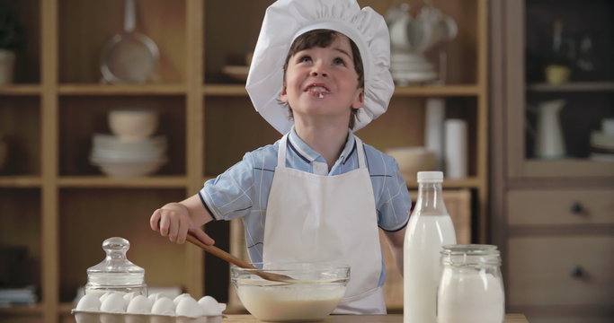 Cute little kitchen-boy making batter and enjoying its taste 