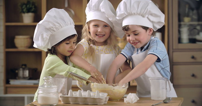 Three lovely kids trying to knead dough in cooking class 
