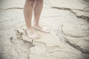 Man legs and feet standing on the sand of the beach, summer time