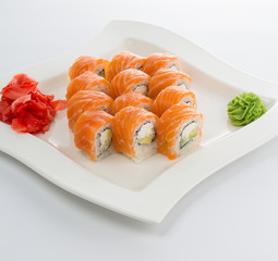 Salmon (philadelphia) sushi roll on a white plate with ginger and wasabi