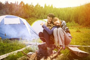 Fototapeta premium Portrait of happy couple sitting near by the campfire with the tents on background, Montenegro 
