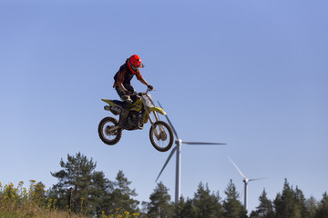 A motorcycle jumper in the air an two wind turbines in the background