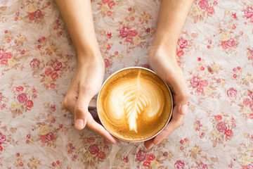 Vintage woman hands holding latte art coffee mug on flower vinta