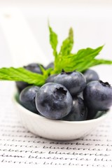 Blueberries with mint in porcelain spoon on text background