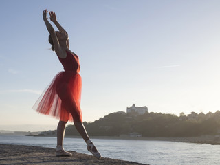 ballerina dancing outdoors in red dress, with the city and sea in background