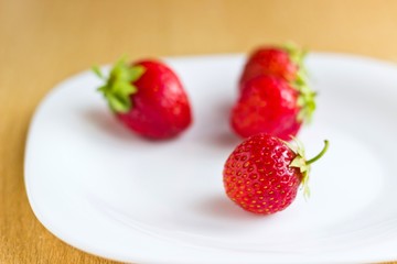 Fresh ripe strawberries on white dish. Focus on foreground