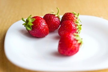 Fresh ripe strawberries on white dish. Focus on background