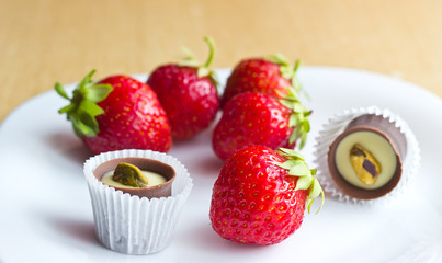 Fresh ripe strawberries and chocolate candy on white dish. Focus on foreground