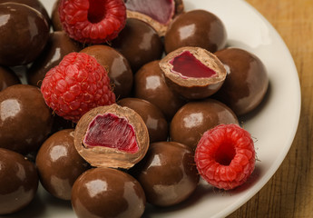 Milk chocolate coated jelly candies and fresh raspberry on white