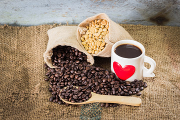 coffee cup and coffee beans on burlap textile and brown background.