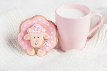 Pink gingerbread sheep with cup of milk on white knitted backgro