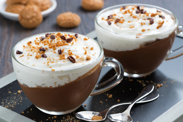 chocolate dessert with cream and amaretti in cups on black board