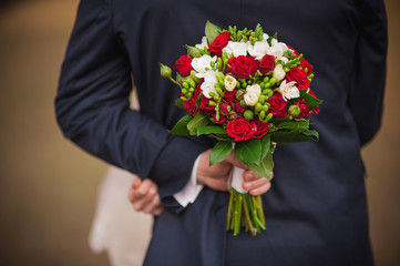 Elegant bride and groom holding bouquet behind his back