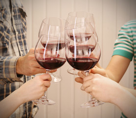 Clinking glasses of red wine in hands on color wooden planks background