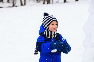 Fototapeta na wymiar cute little boy building snowman in winter