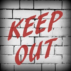 The words Keep Out in red text on a brick wall background. Processed in black and white with a vignette added for effect