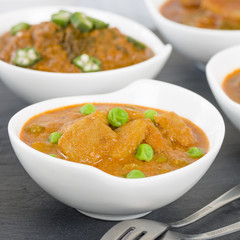 Aloo Matar - Potatoes and green peas cooked in a mild creamy tomato gravy. Chapattis and other vegetarian curries on background.
