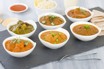 Vegetarian Curries - Selection of South Asian vegetarian curries in white bowls. Paneer Makhani, Palak Paneer, Aloo Matar, Baigan Bharta, Chilli Potatoes and Bhindi Masala, Pilau Rice and Chapattis.

