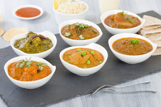 Vegetarian Curries - Selection of South Asian vegetarian curries in white bowls. Paneer Makhani, Palak Paneer, Aloo Matar, Baigan Bharta, Chilli Potatoes and Bhindi Masala, Pilau Rice and Chapattis.
