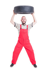 Smiling mechanic lifting a car wheel above head.