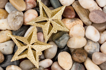 Fototapeta na wymiar Christmas star ornaments on pebbles - Gold glitter star ornaments set on multi colored stones as Christmas background.