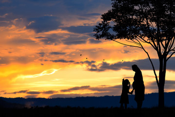 A silhouette of a happy family, mother,girl and infant (women pregnancy) with tree on blurred sunset sky on mountain
