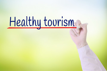Doctor hand with Glove writing Health tourism over green blurred background