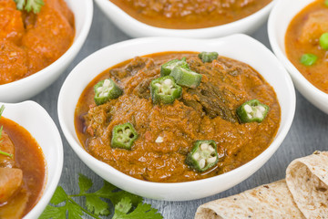 Bhindi Masala - Spiced okra in thick gravy. Chapattis and other vegetarian curries on background.
