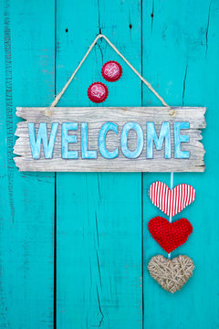 Welcome sign with hearts and bottle caps hanging on teal blue door
