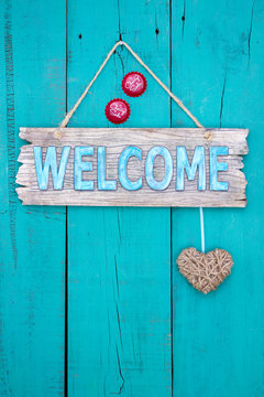 Welcome sign with heart  and bottle caps hanging on teal blue door