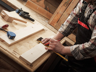 Carpenter marking a measurement on a wooden plank.