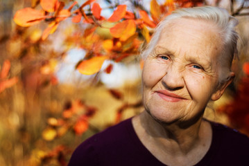 Portrait of the smiling elderly woman. A photo on the autumn background