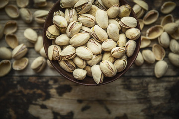 salted pistachios in a wooden bowl on wooden rustic background, top view