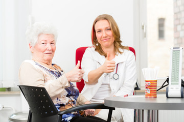 Junge Ärztin sitzt mit Rentnerin in Praxis Sprechstunde am Schreibtisch