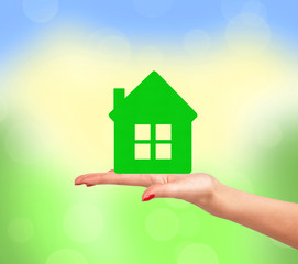 Female hand with small model of house over bright nature backgro