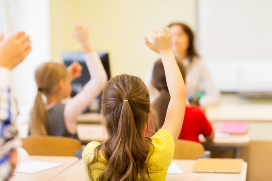 Group Of School Kids Raising Hands In Classroom